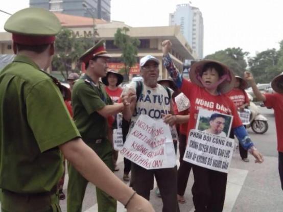 Cấn Thị Thêu phản đối công an sử dụng bạo lực. Bà mang trên tay bức hình con trai là Trịnh Bá Tư bị côn đồ thân chính quyền tấn công vào tháng Sáu năm 2015. © private.